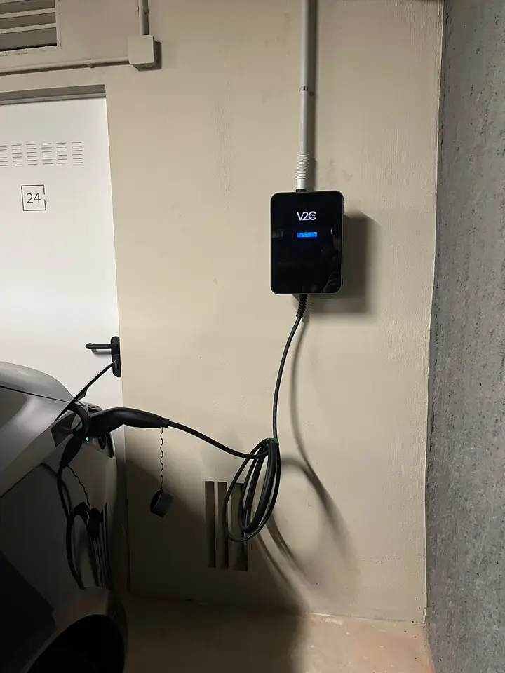 Cargador V2C Trydan junto a una plaza de garaje con el cable conectado al coche eléctrico