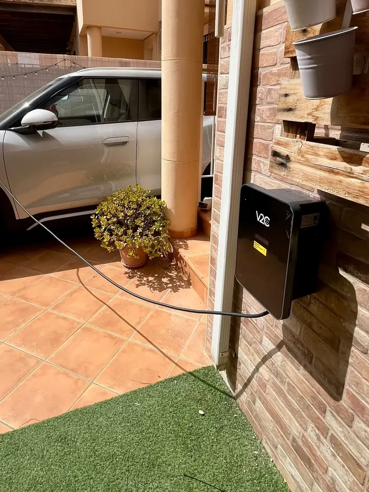 Cargador V2C Trydan en la pared de un patio de vivienda con el coche aparcado al lado